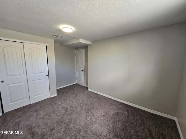 unfurnished bedroom featuring a closet, dark carpet, and a textured ceiling