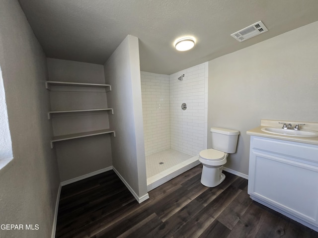 bathroom featuring vanity, toilet, wood-type flooring, and tiled shower