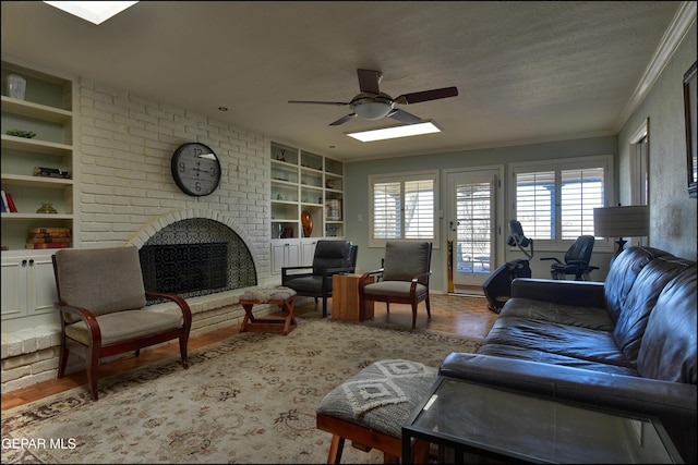 living room featuring ornamental molding, ceiling fan, a brick fireplace, a textured ceiling, and built in features