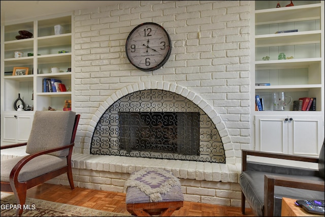 sitting room featuring a brick fireplace, built in features, and parquet floors