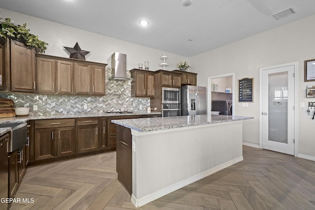 kitchen featuring a center island, wall chimney exhaust hood, light stone countertops, stainless steel appliances, and light parquet flooring