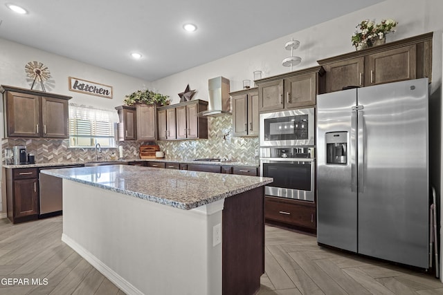 kitchen featuring a center island, wall chimney range hood, appliances with stainless steel finishes, light stone counters, and light parquet flooring