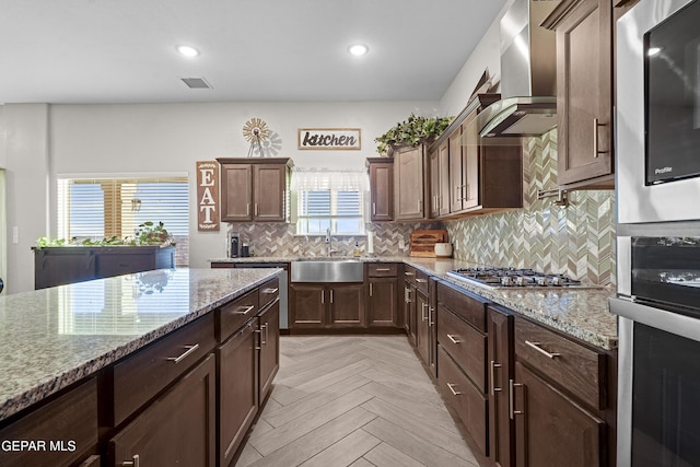 kitchen featuring sink, wall chimney exhaust hood, stainless steel gas cooktop, light stone counters, and light parquet floors