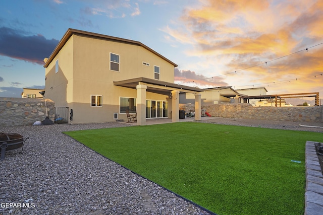 back house at dusk featuring a patio area and a yard