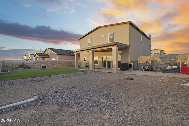 back house at dusk featuring a lawn and a patio