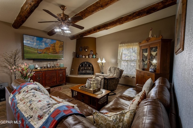 living room featuring ceiling fan, a large fireplace, wood-type flooring, and beam ceiling