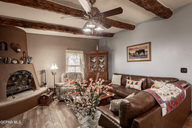 living room featuring hardwood / wood-style floors, beam ceiling, ceiling fan, and a wood stove