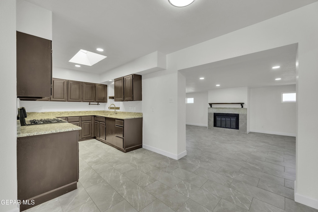 kitchen with stove, a skylight, dark brown cabinetry, sink, and a fireplace