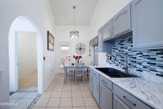 kitchen with sink, light stone counters, decorative light fixtures, decorative backsplash, and light tile patterned flooring