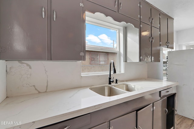 kitchen with light stone countertops, light wood-type flooring, and sink