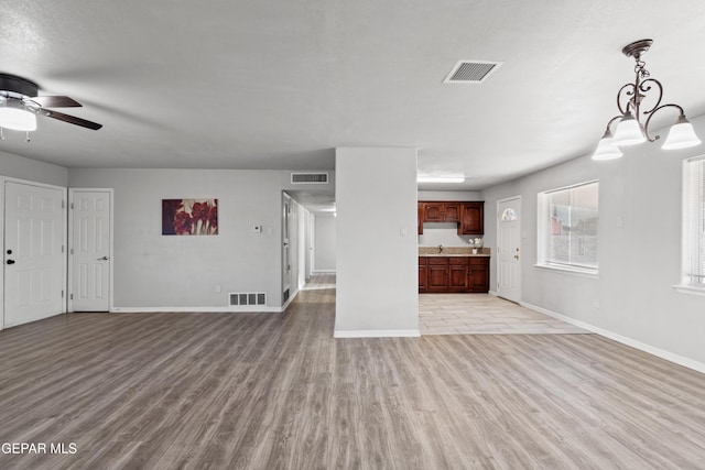 unfurnished living room with ceiling fan with notable chandelier and light hardwood / wood-style floors