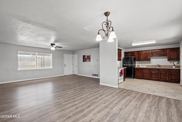 kitchen with black refrigerator, light wood-type flooring, white range with electric cooktop, hanging light fixtures, and dark brown cabinetry