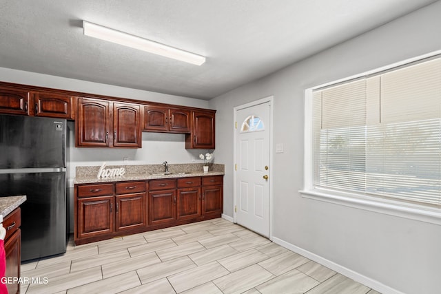 kitchen featuring sink, black refrigerator, and light stone countertops