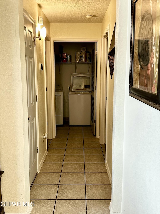 hall with light tile patterned flooring, independent washer and dryer, and a textured ceiling