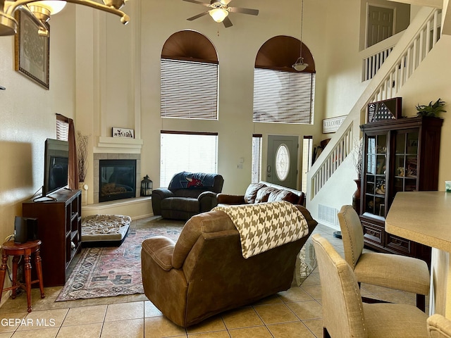 tiled living room with ceiling fan, a fireplace, and a towering ceiling