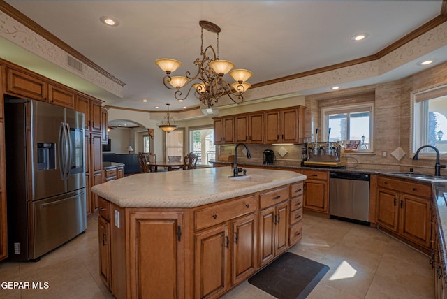 kitchen with appliances with stainless steel finishes, a kitchen island with sink, sink, pendant lighting, and an inviting chandelier