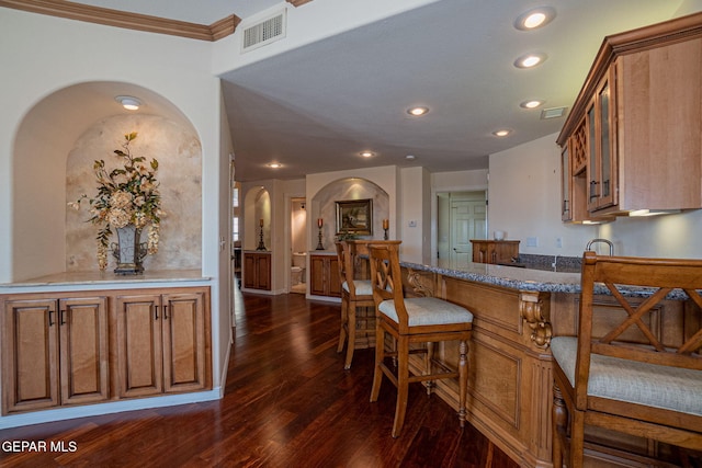 kitchen featuring a kitchen bar, dark hardwood / wood-style floors, light stone counters, and crown molding