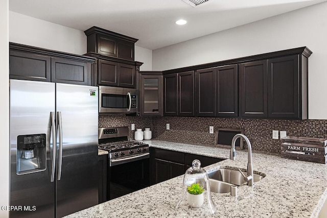 kitchen featuring backsplash, sink, light stone countertops, appliances with stainless steel finishes, and dark brown cabinetry