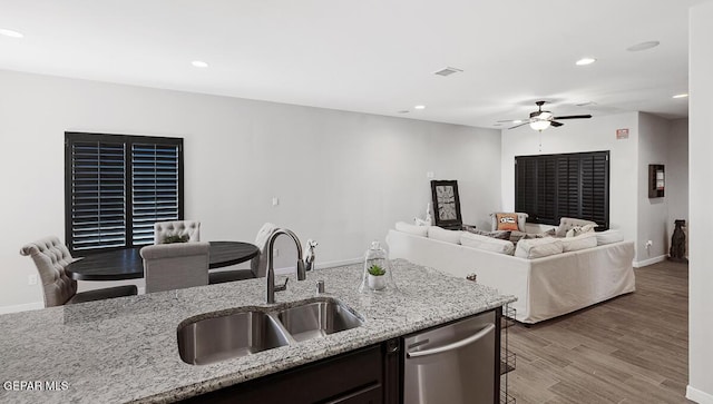 kitchen featuring light stone countertops, sink, ceiling fan, stainless steel dishwasher, and hardwood / wood-style floors