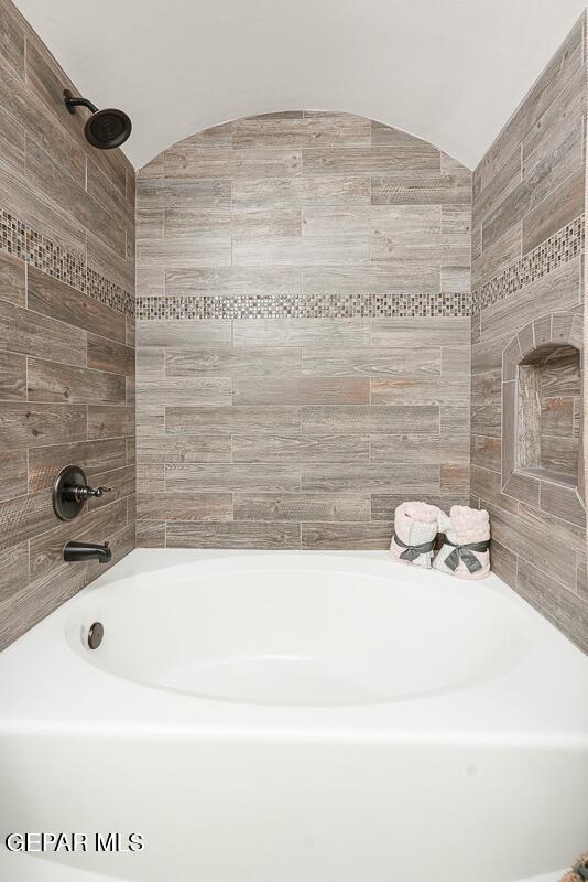 bathroom featuring lofted ceiling and tiled shower / bath