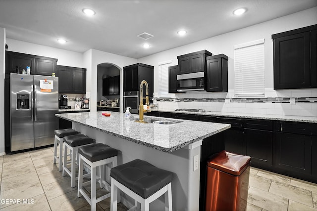 kitchen with light stone counters, a breakfast bar, stainless steel appliances, sink, and an island with sink