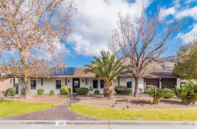 ranch-style house with a front yard, solar panels, and a garage