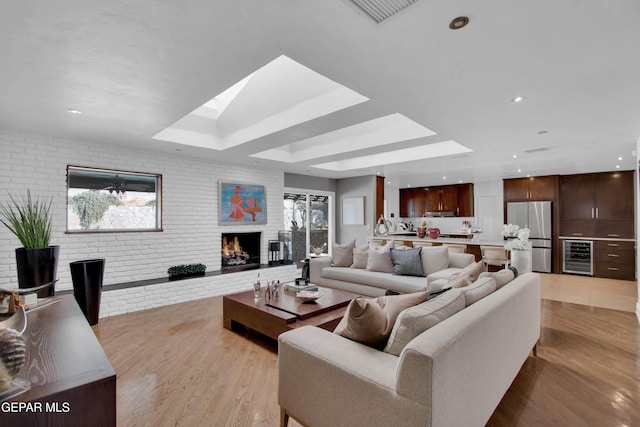 living room featuring wine cooler, a fireplace, brick wall, and light wood-type flooring