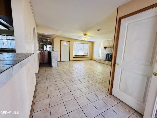 unfurnished living room featuring a fireplace, light tile patterned floors, and ceiling fan