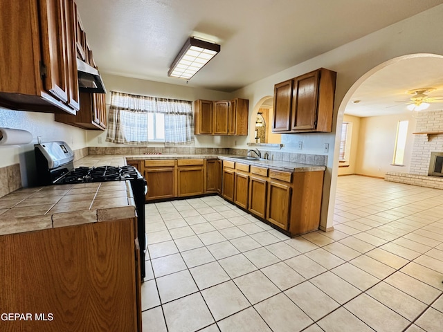 kitchen featuring sink, gas range, ceiling fan, light tile patterned floors, and a fireplace