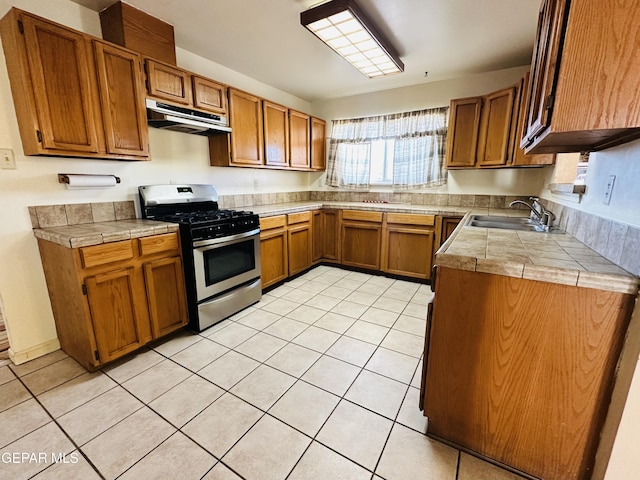 kitchen with tile counters, light tile patterned flooring, sink, and stainless steel gas range