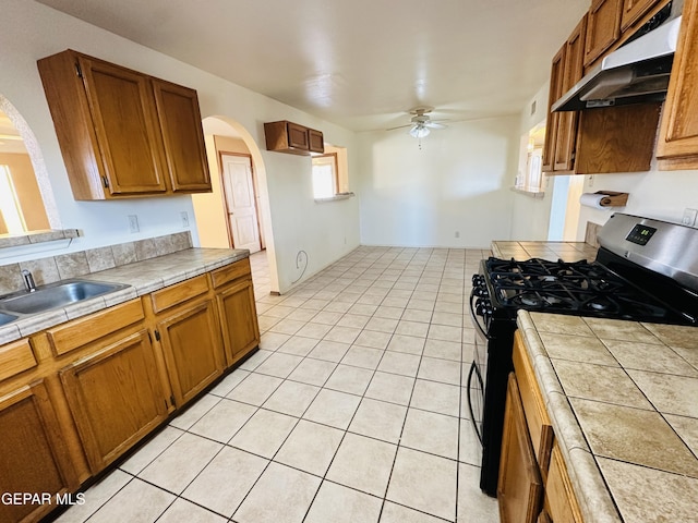 kitchen with black range with gas stovetop, ceiling fan, sink, light tile patterned floors, and tile counters