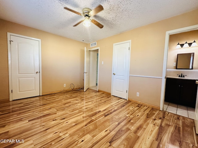 unfurnished bedroom featuring ensuite bath, ceiling fan, a textured ceiling, and light wood-type flooring