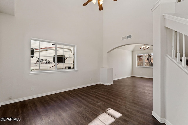 unfurnished living room featuring high vaulted ceiling, dark wood-type flooring, and ceiling fan with notable chandelier