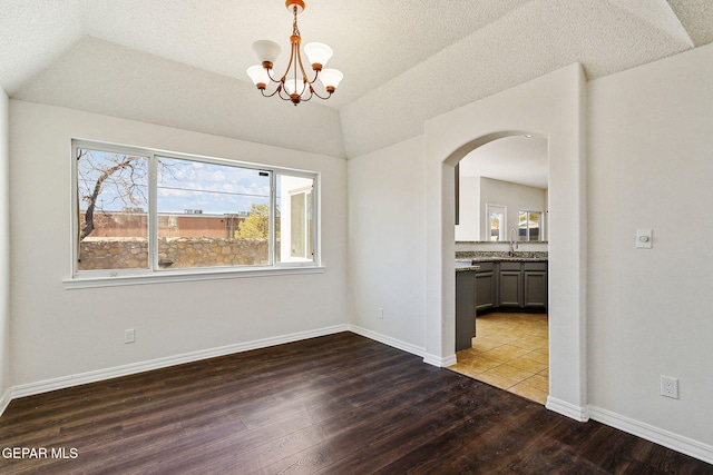 unfurnished dining area featuring hardwood / wood-style flooring, sink, lofted ceiling, and an inviting chandelier