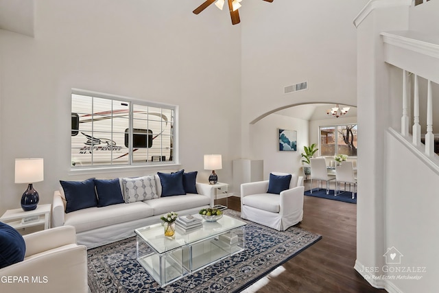 living room with ceiling fan with notable chandelier, a high ceiling, and dark hardwood / wood-style floors