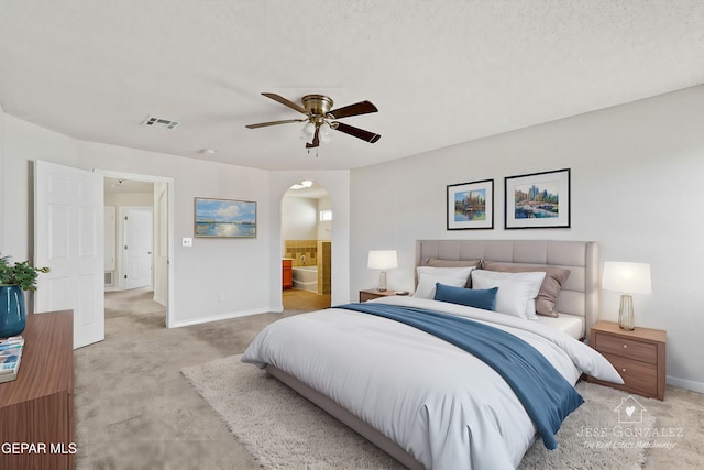 bedroom with ceiling fan, a textured ceiling, ensuite bathroom, and light carpet