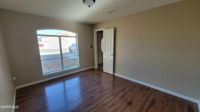 spare room featuring dark hardwood / wood-style floors, a textured ceiling, and a wealth of natural light