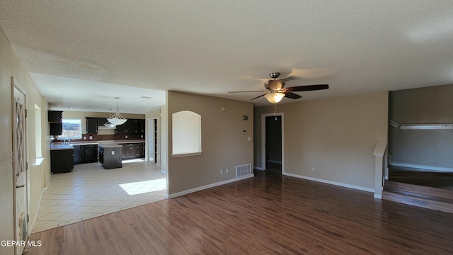 unfurnished living room featuring ceiling fan, wood-type flooring, and a textured ceiling