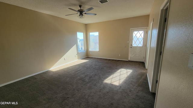 empty room with a textured ceiling, dark carpet, and ceiling fan