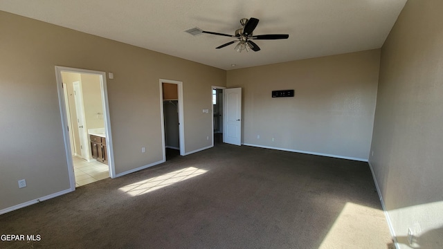 unfurnished bedroom with carpet, ceiling fan, a spacious closet, connected bathroom, and a closet