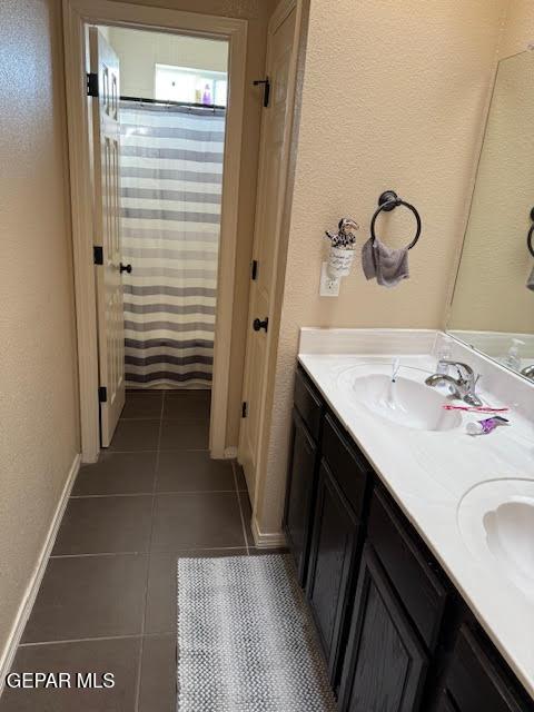 bathroom featuring tile patterned flooring, a shower with shower curtain, a sink, baseboards, and double vanity