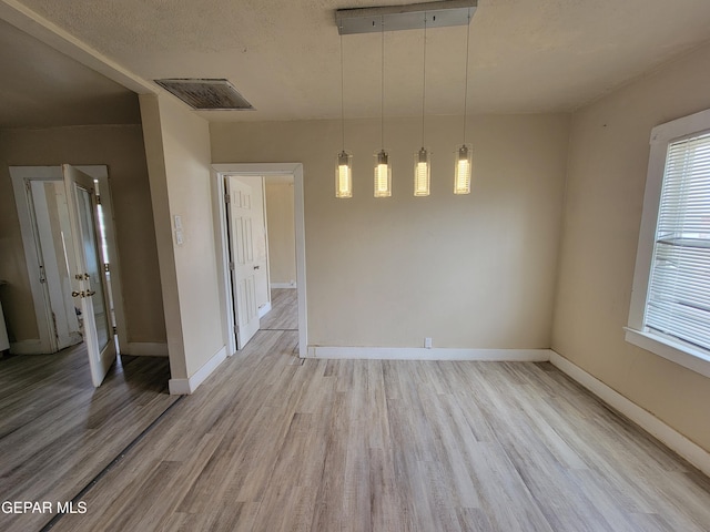 unfurnished dining area with light hardwood / wood-style floors and a textured ceiling