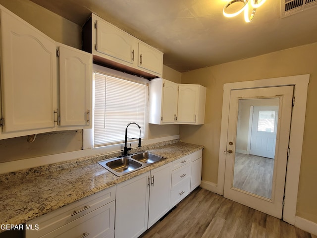 kitchen with light stone counters, sink, white cabinets, and light hardwood / wood-style flooring