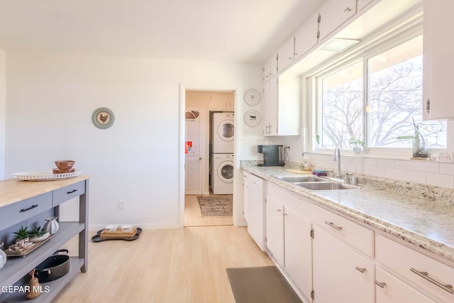 kitchen with stacked washer / dryer, decorative backsplash, sink, and white cabinets