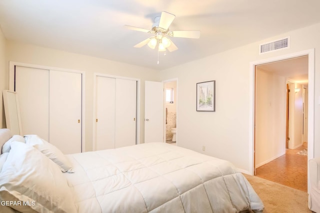 carpeted bedroom featuring multiple closets, ceiling fan, and ensuite bath