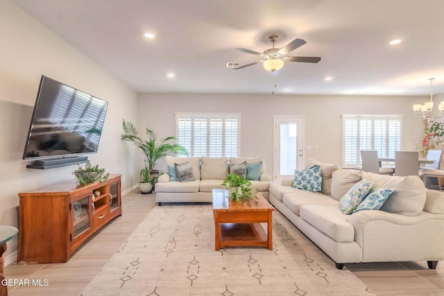 living room with ceiling fan with notable chandelier, light hardwood / wood-style floors, and plenty of natural light