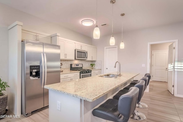 kitchen with light stone countertops, hanging light fixtures, stainless steel appliances, a center island with sink, and sink