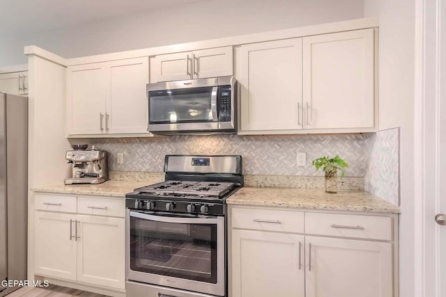 kitchen with stainless steel appliances, light stone countertops, white cabinets, and tasteful backsplash