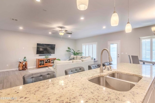 kitchen featuring ceiling fan, a wealth of natural light, light stone counters, sink, and decorative light fixtures