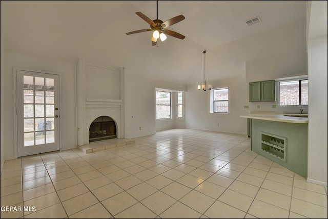 unfurnished living room featuring light tile patterned flooring, sink, high vaulted ceiling, a brick fireplace, and ceiling fan with notable chandelier